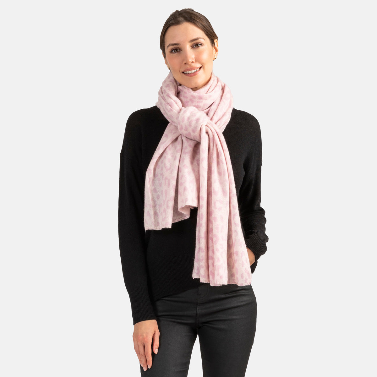 Picture of a woman wearing an oversized knitted cashmere travel wrap or scarf with a cheetah pattern in pink tones.
