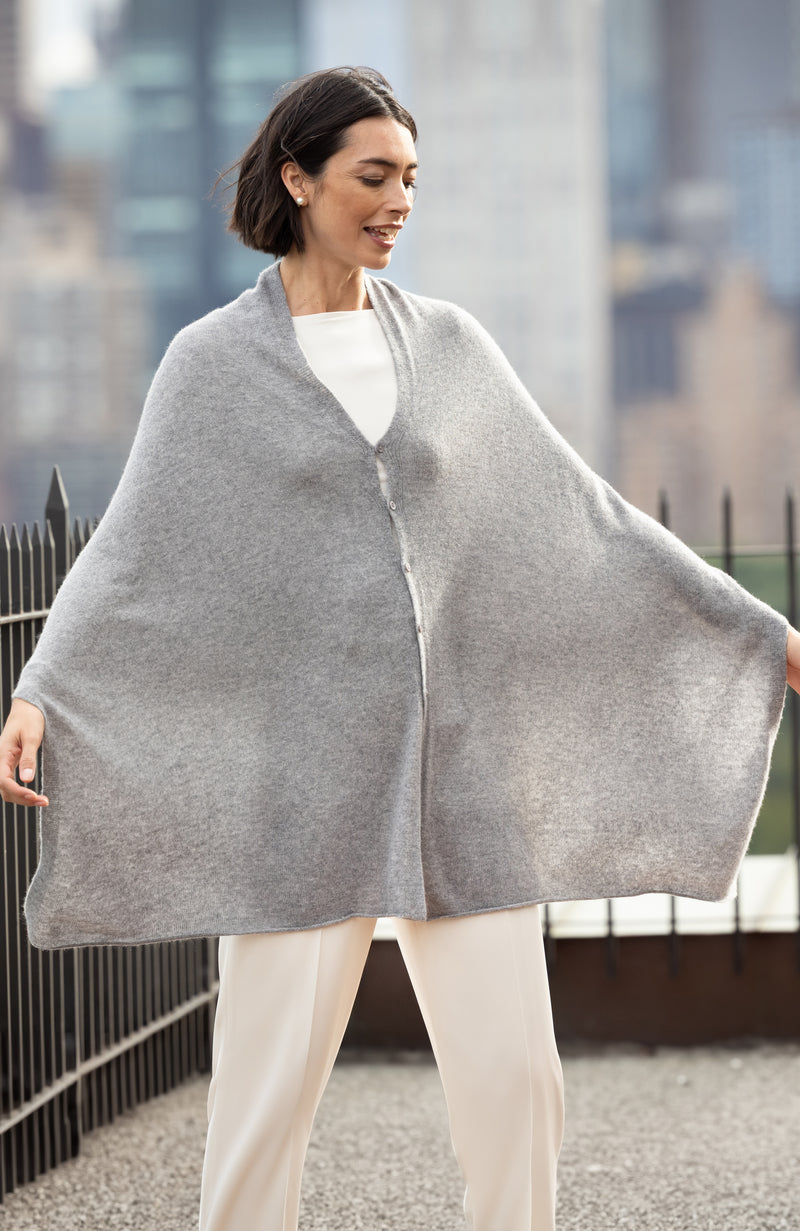 Woman wearing a CASHMERE BUTTON SHOULDER PONCHO + WRAP in medium grey with a blurred cityscape background