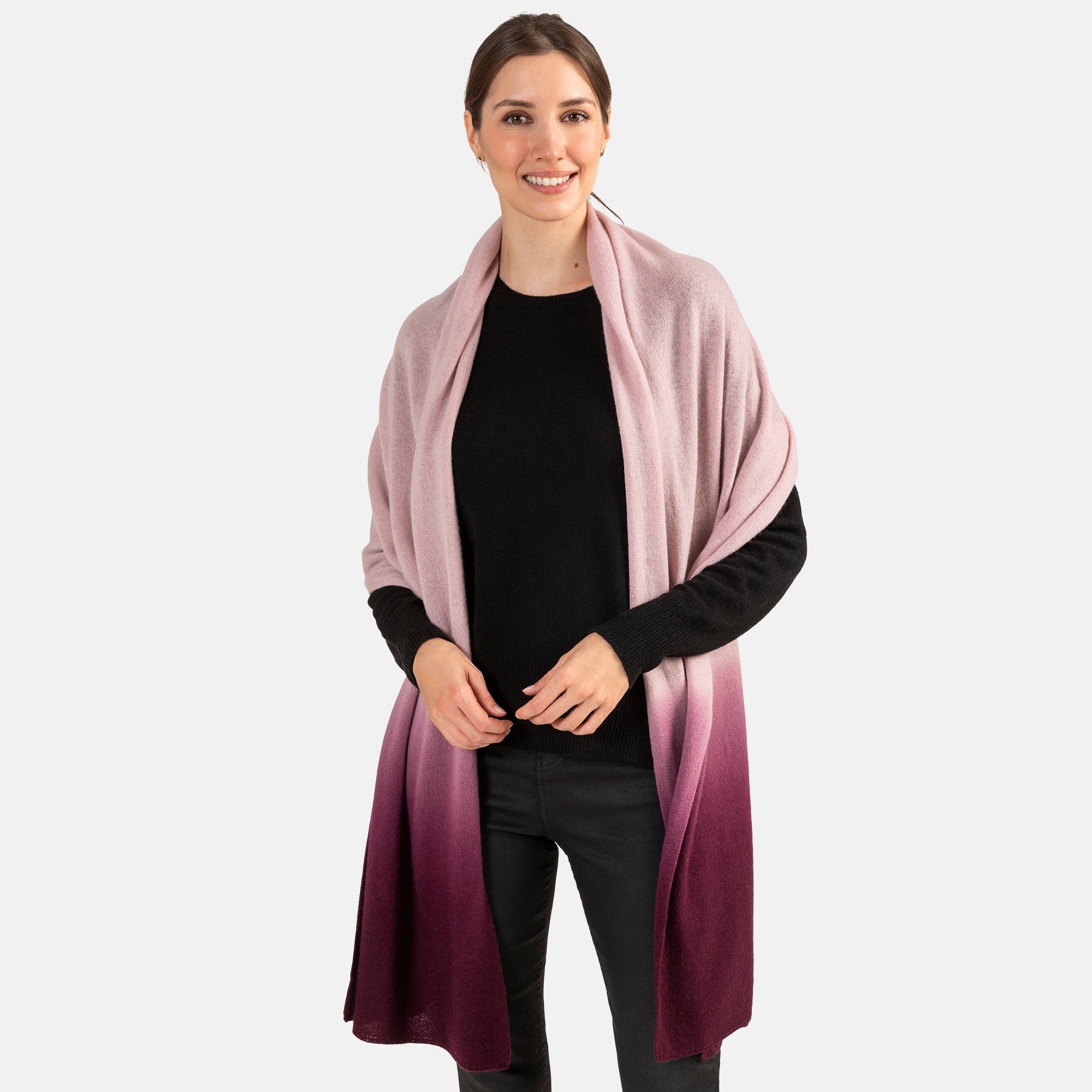 Picture of a woman wearing an oversized knitted cashmere travel wrap or scarf with an ombre pattern in pink and burgundy.  [Dusty Rose/Bordeaux]