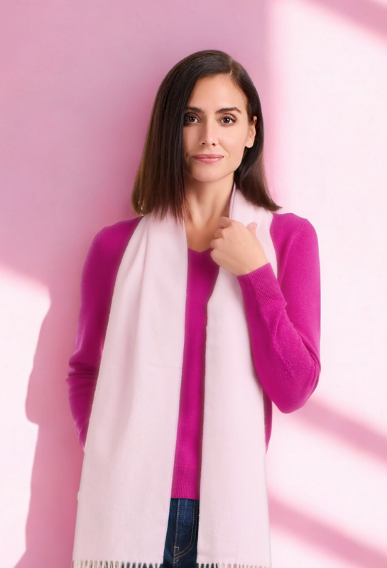 Woman standing against pink wall wearing pink scarf and sweater, vertical