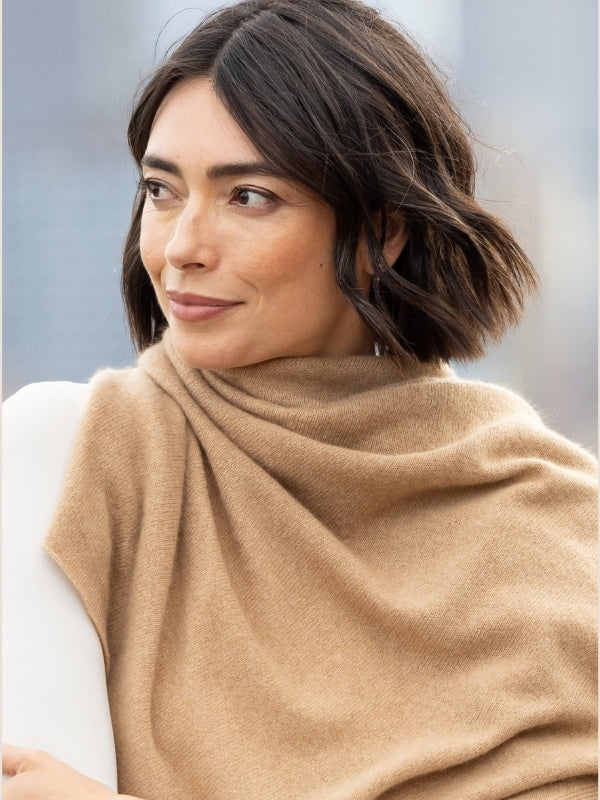 A woman with short dark brown hair is shown in a close-up portrait, wearing a soft camel-colored knit shawl draped over her shoulders.