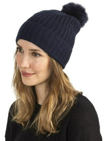 Woman wearing a black cashmere beanie with shearling pom, rib knit detail.