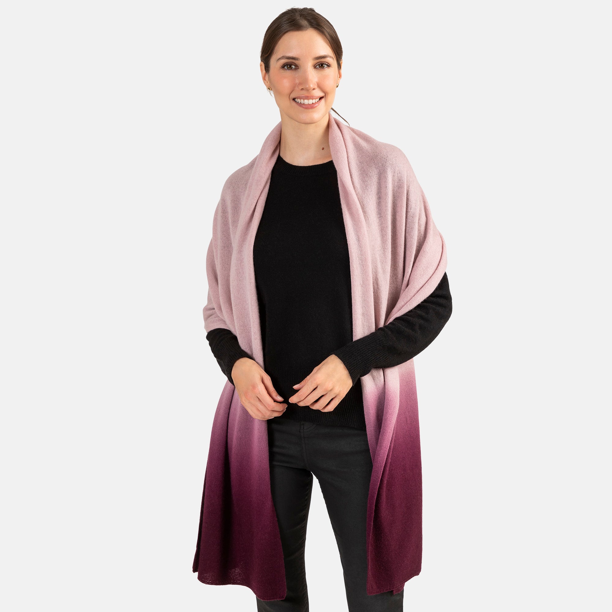 Picture of a woman wearing an oversized knitted cashmere travel wrap or scarf with an ombre pattern in pink and burgundy.  