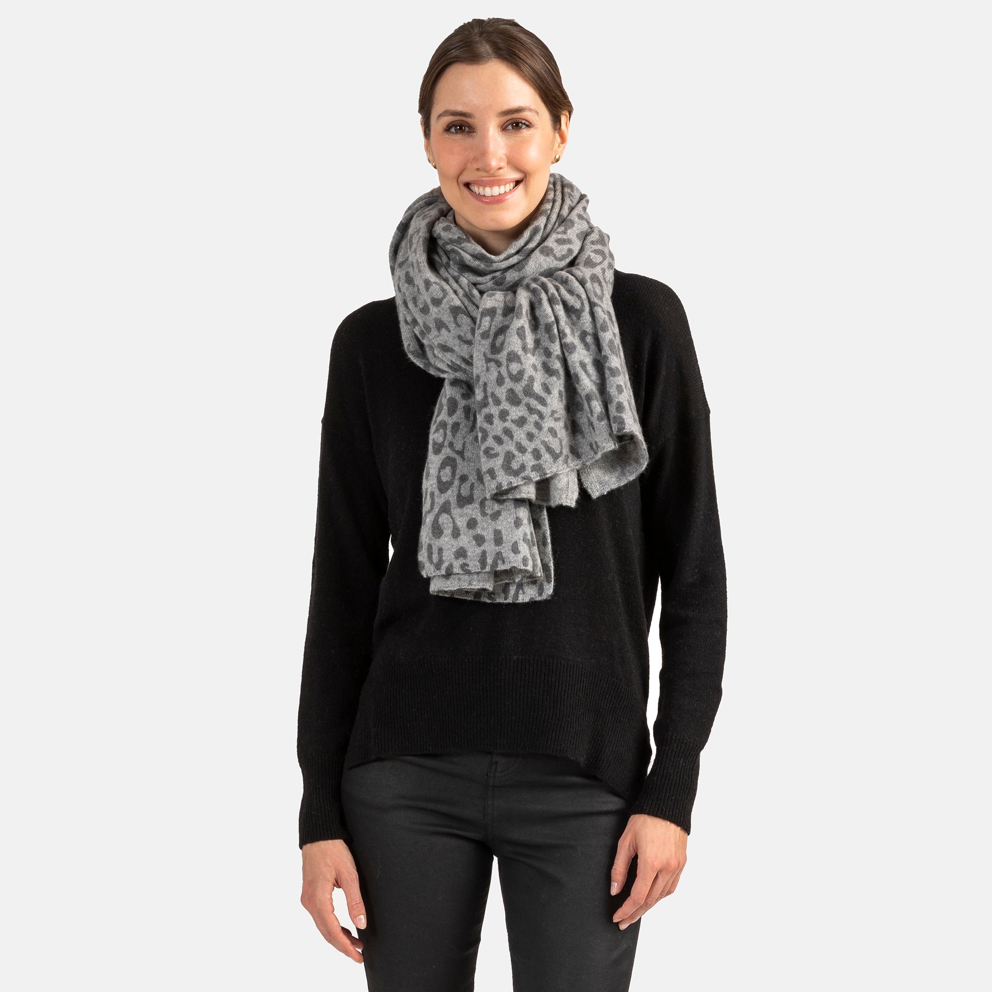 Picture of a woman wearing an oversized knitted cashmere travel wrap or scarf with a cheetah pattern in grey tones.