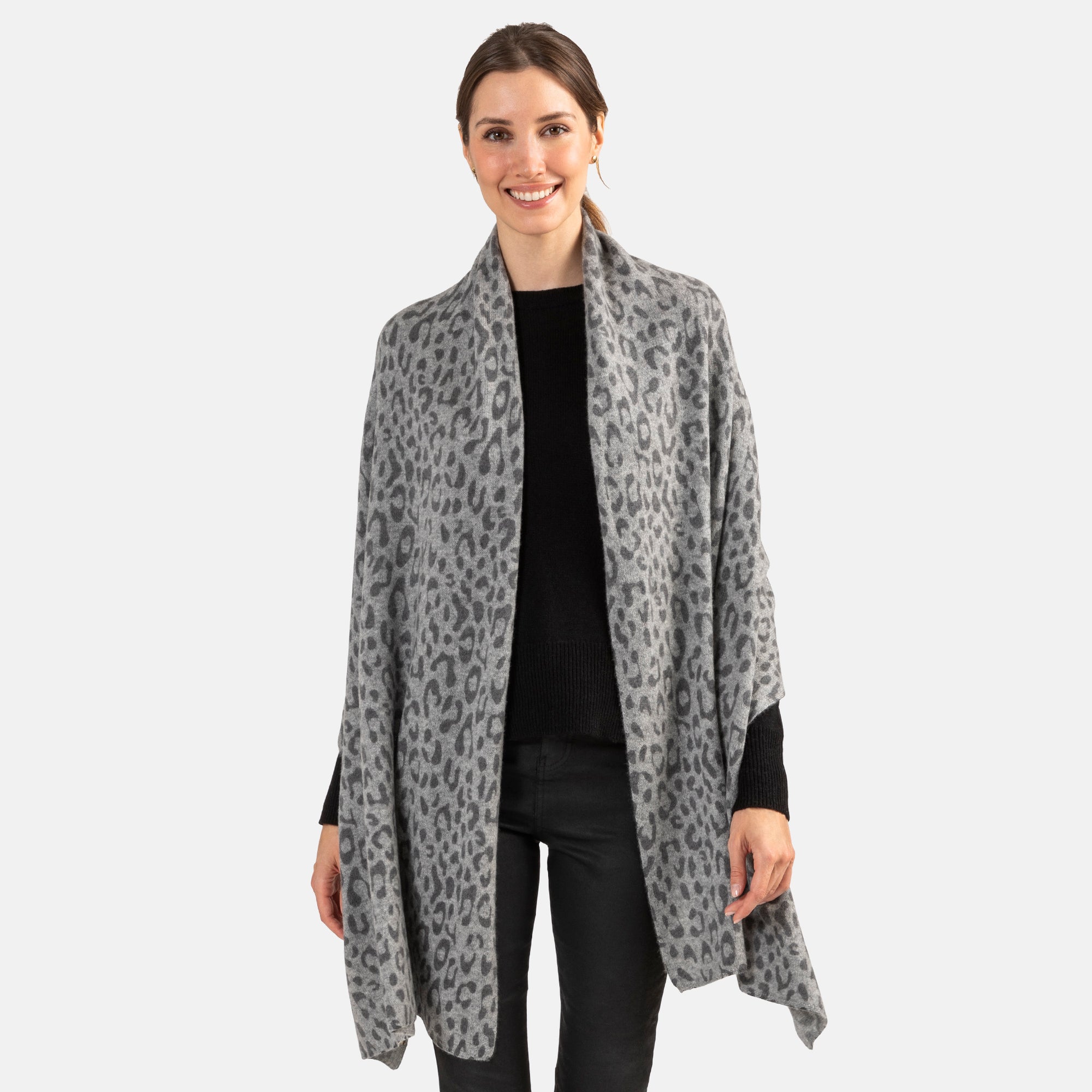Picture of a woman wearing an oversized knitted cashmere travel wrap or scarf with a cheetah pattern in grey tones.