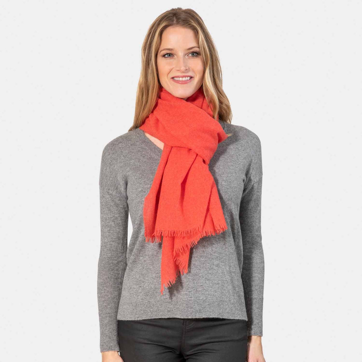 Picture of a woman wearing a lightweight oversized cashmere scarf with eyelash fringe, coral.