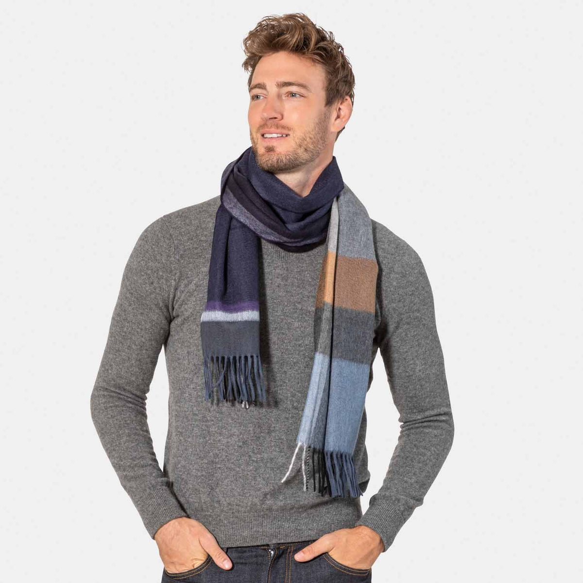 Picture of a man wearing an cashmere color block scarf with fringe in blues, greys and browns.